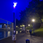 a blue light phone is illuminated at dusk near the tennis courts by the Women's Building